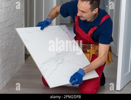 A male construction worker installs a large ceramic tile  Stock Photo