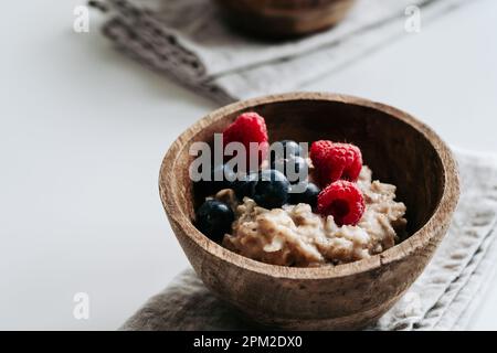 Oatmeal porridge with fresh blueberry, raspberry berries fruits in wooden bowl on linen  cloth, close up. Healthy food, breakfast Stock Photo