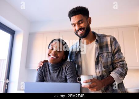 Young Couple At Home Looking At Laptop On Counter In Kitchen Together Stock Photo