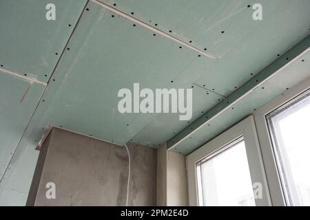 Installation of drywall. Workers are using screws and a screwdriver to attach plasterboard to the ceiling Stock Photo
