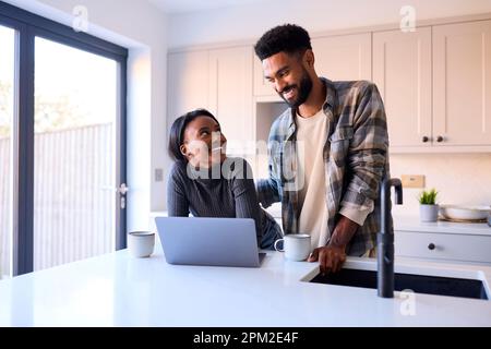 Young Couple At Home Looking At Laptop On Counter In Kitchen Together Stock Photo