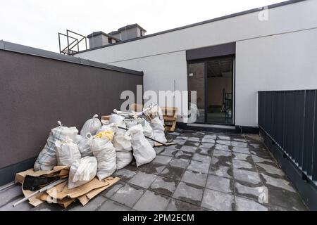construction debris on the street near a house . Wooden window frame and bags of cement, sand and garbage. The concept of construction and repair in Stock Photo