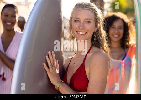 Portrait of happy diverse female friends holding surfboards and smiling at beach, with copy space Stock Photo