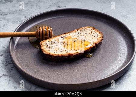 Slice of cake bread with walnuts and honey dipper on ceramic plate on gray background, close up Stock Photo
