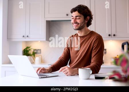 Portrait Of Young Man At Home Working On Laptop On Counter In Kitchen Stock Photo