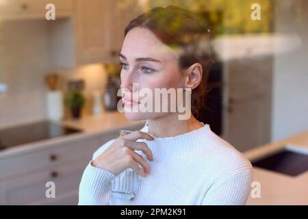 Thoughtful Young Woman At Home In Kitchen Looking Out Through Window Stock Photo