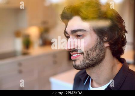 Smiling Young Man At Home In Kitchen Looking Out Through Window Stock Photo