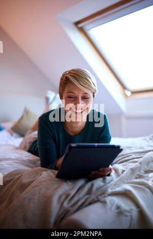 Young Woman Lying On Bed Wearing Pyjamas At Home Looking At Digital Tablet Stock Photo