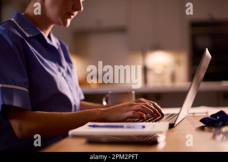 Close Up Of Woman Wearing Medical Scrubs Working Or Studying On Laptop At Home At Night Stock Photo