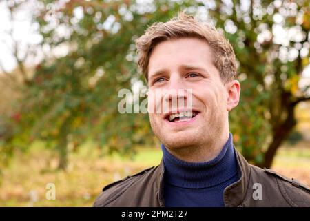 Smiling Young Man Wearing Coat Standing Outside In Autumn Or Winter Countryside Stock Photo