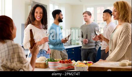 Group Of Friends At Home In Kitchen With Drinks Making Food For Party Stock Photo