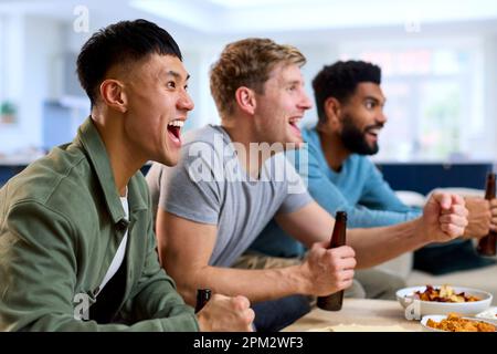 Group Of Excited Male Friends Watching Sports On TV At Home In Lounge Together Stock Photo