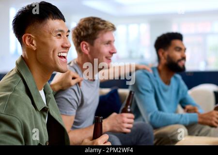 Group Of Excited Male Friends Watching Sports On TV At Home In Lounge Together Stock Photo