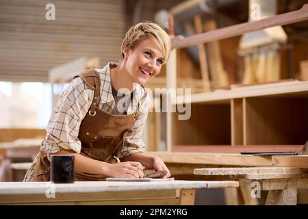 Female Apprentice Working As Carpenter In Furniture Workshop Stock Photo