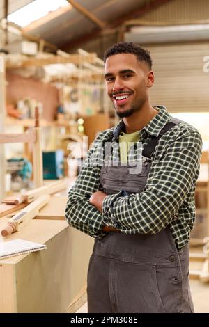 Portrait Of Male Apprentice Working As Carpenter In Furniture Workshop Stock Photo