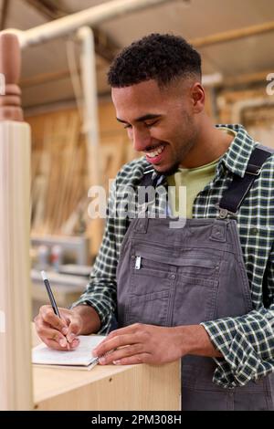 Male Apprentice Working As Carpenter In Furniture Workshop Making Notes Stock Photo