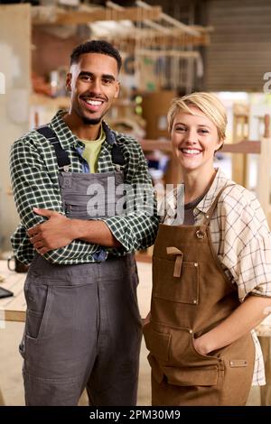 Portrait Of Male And Female Apprentices Working As Carpenters In Furniture Workshop Stock Photo