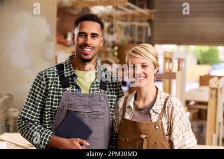 Portrait Of Male And Female Apprentices Working As Carpenters In Furniture Workshop Stock Photo