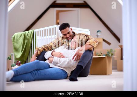 Couple Expecting Baby Relaxing In Nursery Of New Home Together With Moving In Boxes Stock Photo