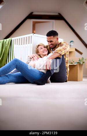 Couple Expecting Baby Relaxing In Nursery Of New Home Together With Moving In Boxes Stock Photo