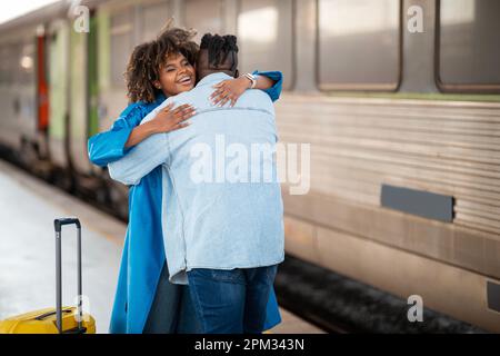 Long-awaited meeting. Joyful excited black couple hugging on platform at railway station Stock Photo