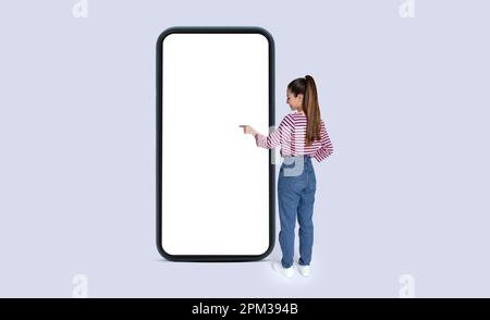 Young long-haired woman touching smartphone white screen, mockup Stock Photo