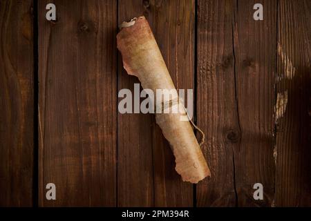 An aged parchment scroll is laid out on a wooden surface. Stock Photo