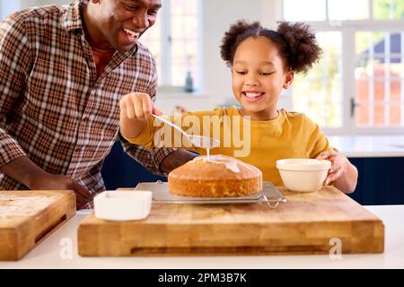 Family Shot With Father And Daughter Baking At Home In Kitchen Decorating Cake With Icing Stock Photo