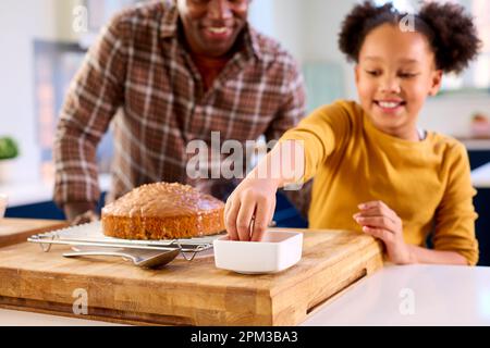 Family Shot With Father And Daughter Baking At Home In Kitchen Decorating Cake With Sprinkles Stock Photo