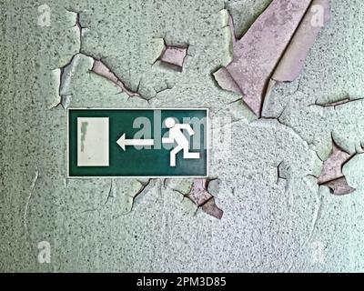 Emergency exit sign in old building on wall with peeling paint Stock Photo