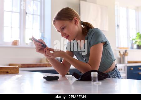 Diabetic Girl At Home Testing For Blood Glucose Level With Monitor Kit In Kitchen Stock Photo