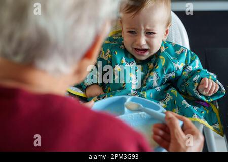 Grandmother feeding her fussy grandson Stock Photo