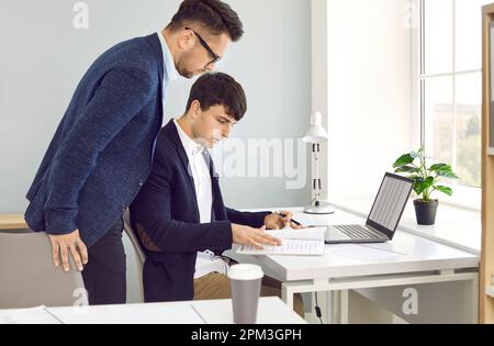 Male colleagues are reviewing document entries together while working in company's business office. Stock Photo