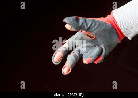 Demaged glove. Defocus worn dirty and leaky gloves. One male hand in worn workers gloves, protection against damage during operation, closeup on backg Stock Photo
