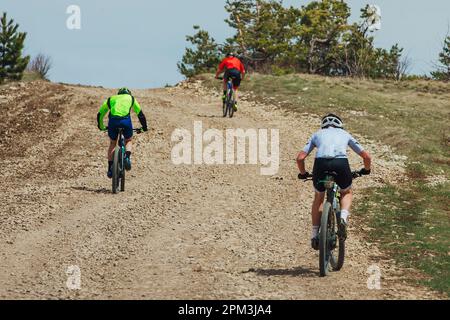 rear view three mountainbikers riding bike uphill, biking on gravel road, cycling competition Stock Photo