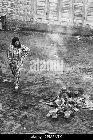 A woman walking past a burning sheep head in Casablanca during Eid. Morocco. Stock Photo