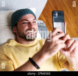 Man using his mobile phone and smiling while relaxing on sofa at home. Stock Photo