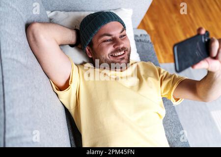 Man lying on sofa at home and watching social media videos. Stock Photo