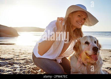 Checking out some new scenery. a mature woman taking her dog for a walk on the beach. Stock Photo