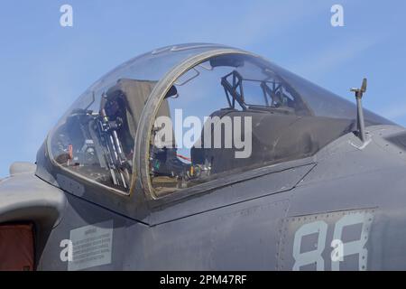 The cockpit and glass canopy of a modern fighter jet attack aircraft is shown on display up close during the day. with a blue sky in the background. Stock Photo