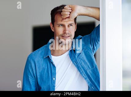 Feeling pensive at home. a handsome man looking pensive while leaning against a door. Stock Photo