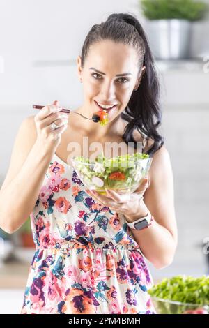 A young woman has a healthy salad for breakfast and stands in her kitchen. Stock Photo