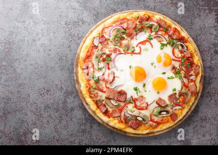 Crispy Aussie pizza with bacon, eggs, peppers, mushrooms, mozzarella and red onions close-up on a wooden board on the table. Horizontal top view from Stock Photo