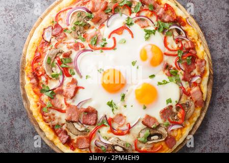 Hot pizza with bacon, eggs, peppers, mushrooms, mozzarella and red onions close-up on a wooden board on the table. Horizontal top view from above Stock Photo