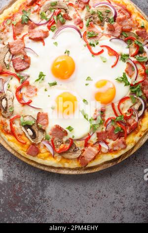 Aussie pizza topped with a base of barbecue sauce, mozzarella cheese, bits of chopped bacon, eggs, peppers and mushrooms closeup on the table. Vertica Stock Photo