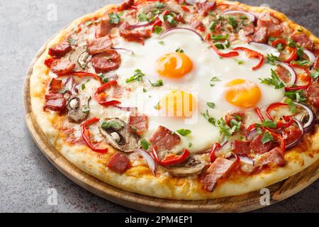 Crispy Aussie pizza with bacon, eggs, peppers, mushrooms, mozzarella and red onions close-up on a wooden board on the table. Horizontal Stock Photo