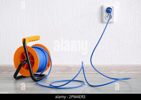 Extension cord reel plugged into socket on white floor indoors