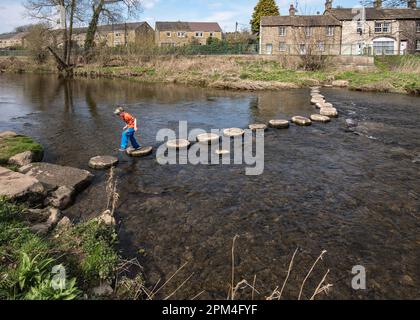 Youngster having fun whilst confidently hopping across the stepping stones across the River Aire at Gargrave in the Yorkshire Dales. Stock Photo