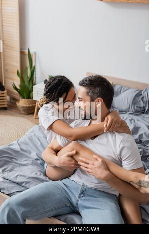 joyful african american woman embracing happy bearded boyfriend while having fun on bed at home,stock image Stock Photo