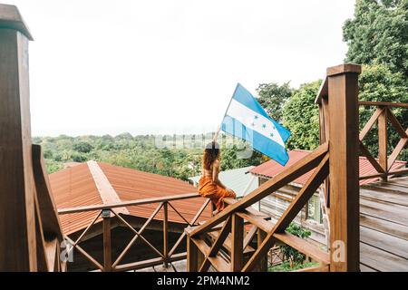 A young woman stands proudly with the Honduran flag in front of a picturesque mountain lodge Stock Photo